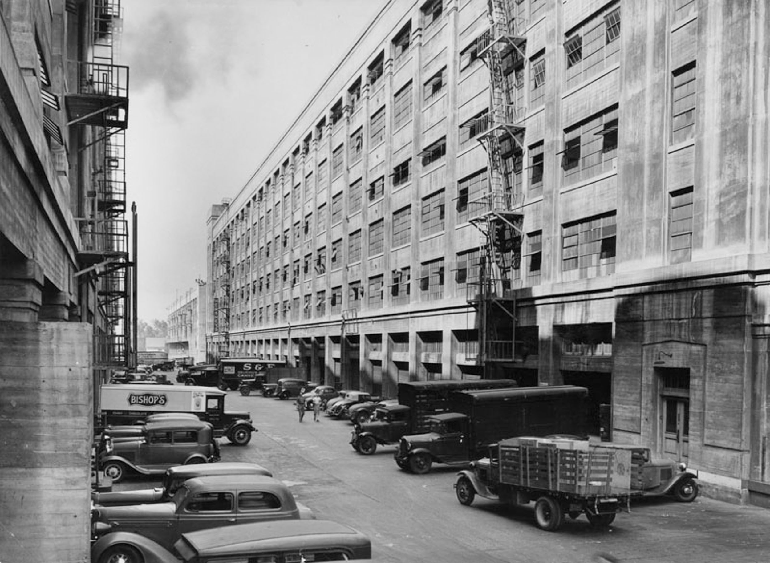 black and white photo of old trucks lined in front of an old building