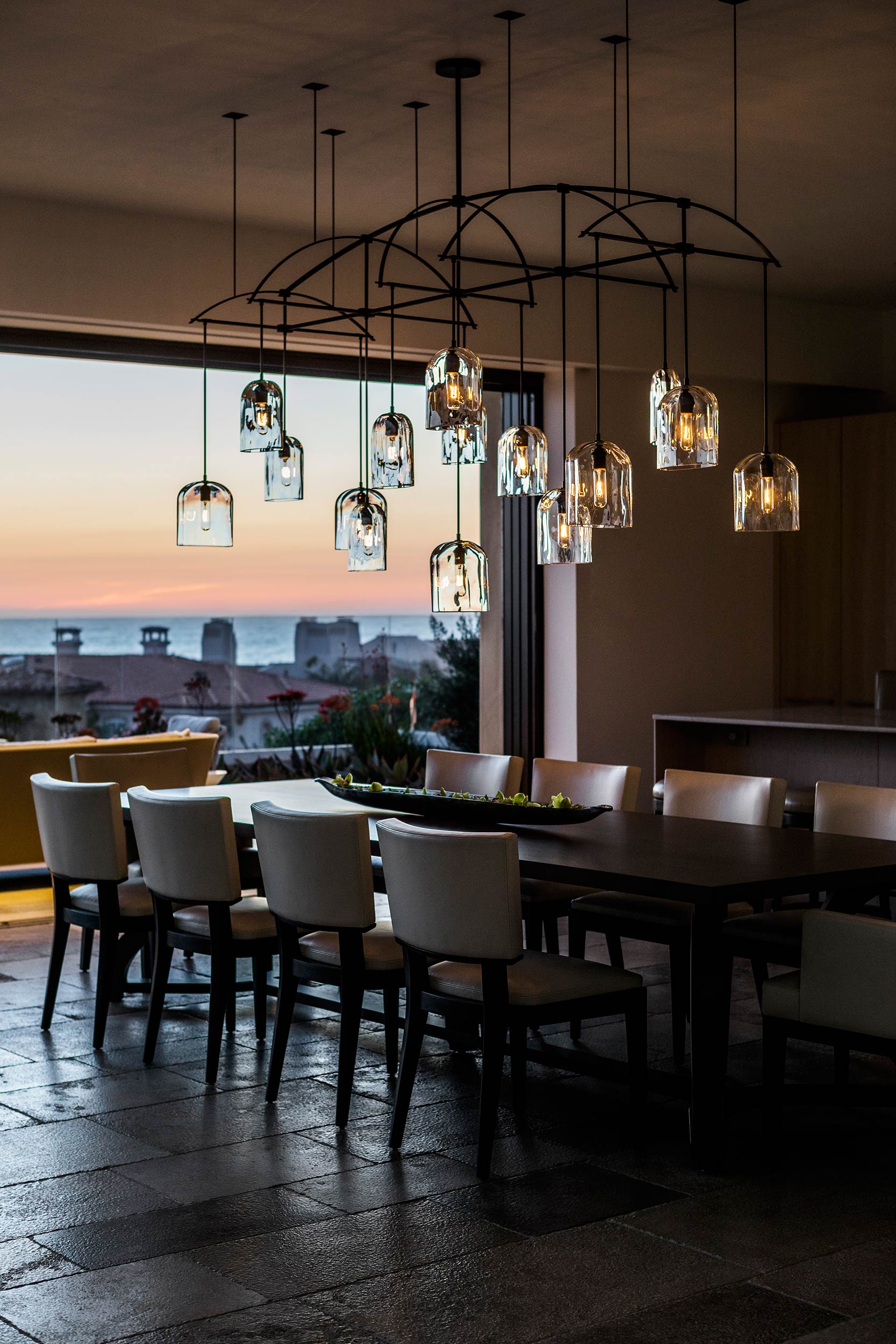 A chandelier over the dining table reflects the dramatic oceanview sunset