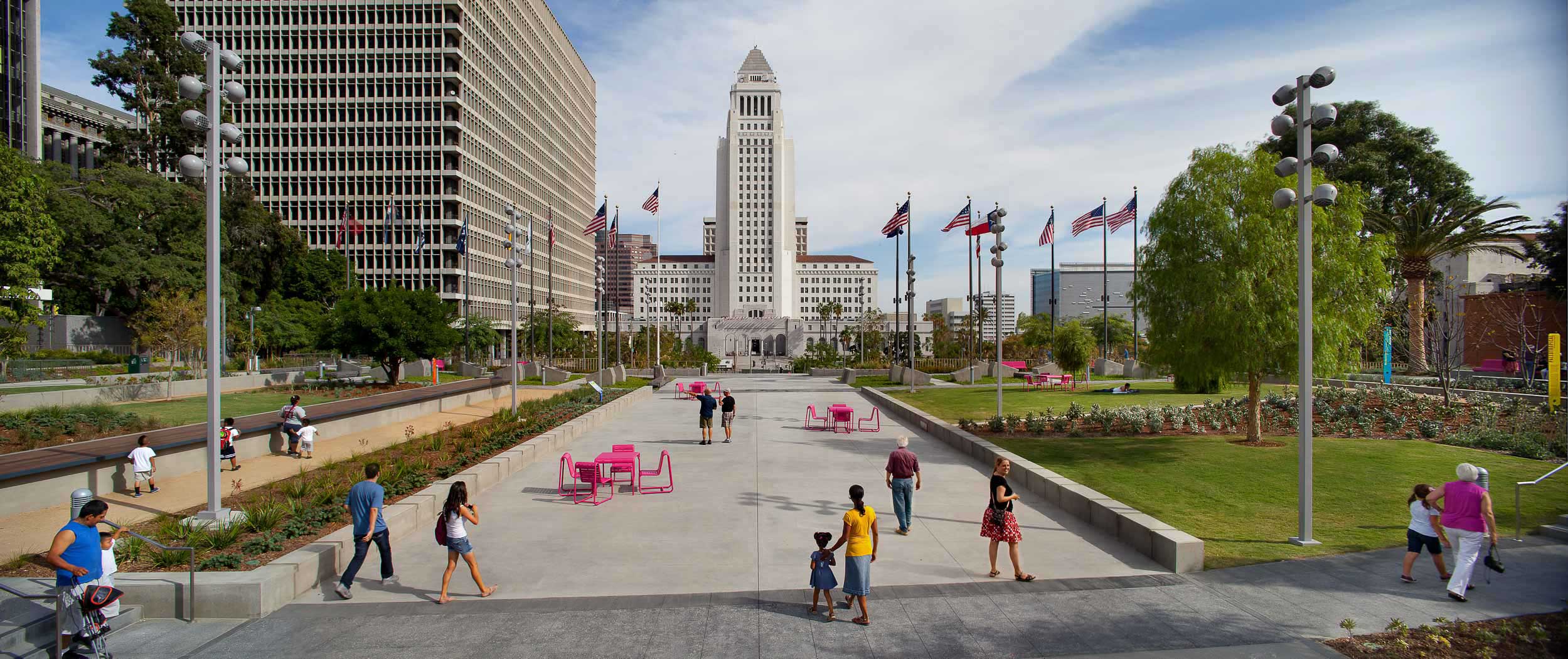 grand park pathway in between grassy lawns with people walking throughout the park and city hall in the center background