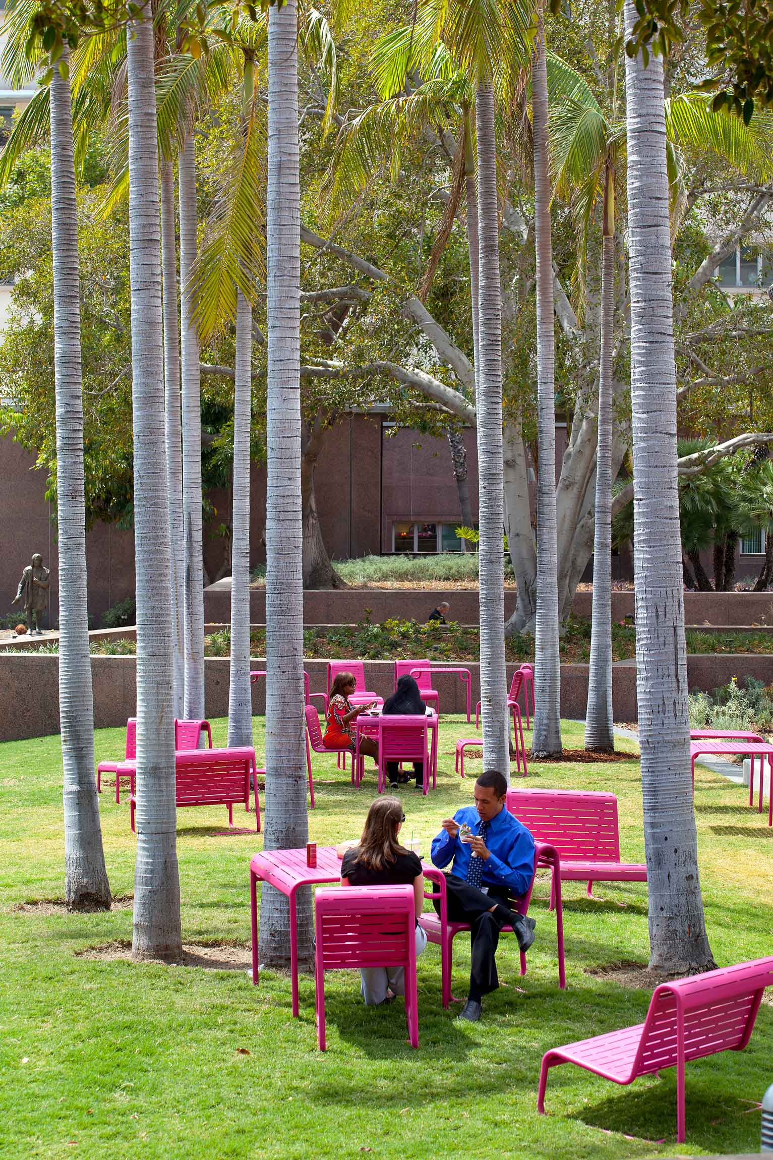 people eating at a pink table set on a grassy lawn under a tree