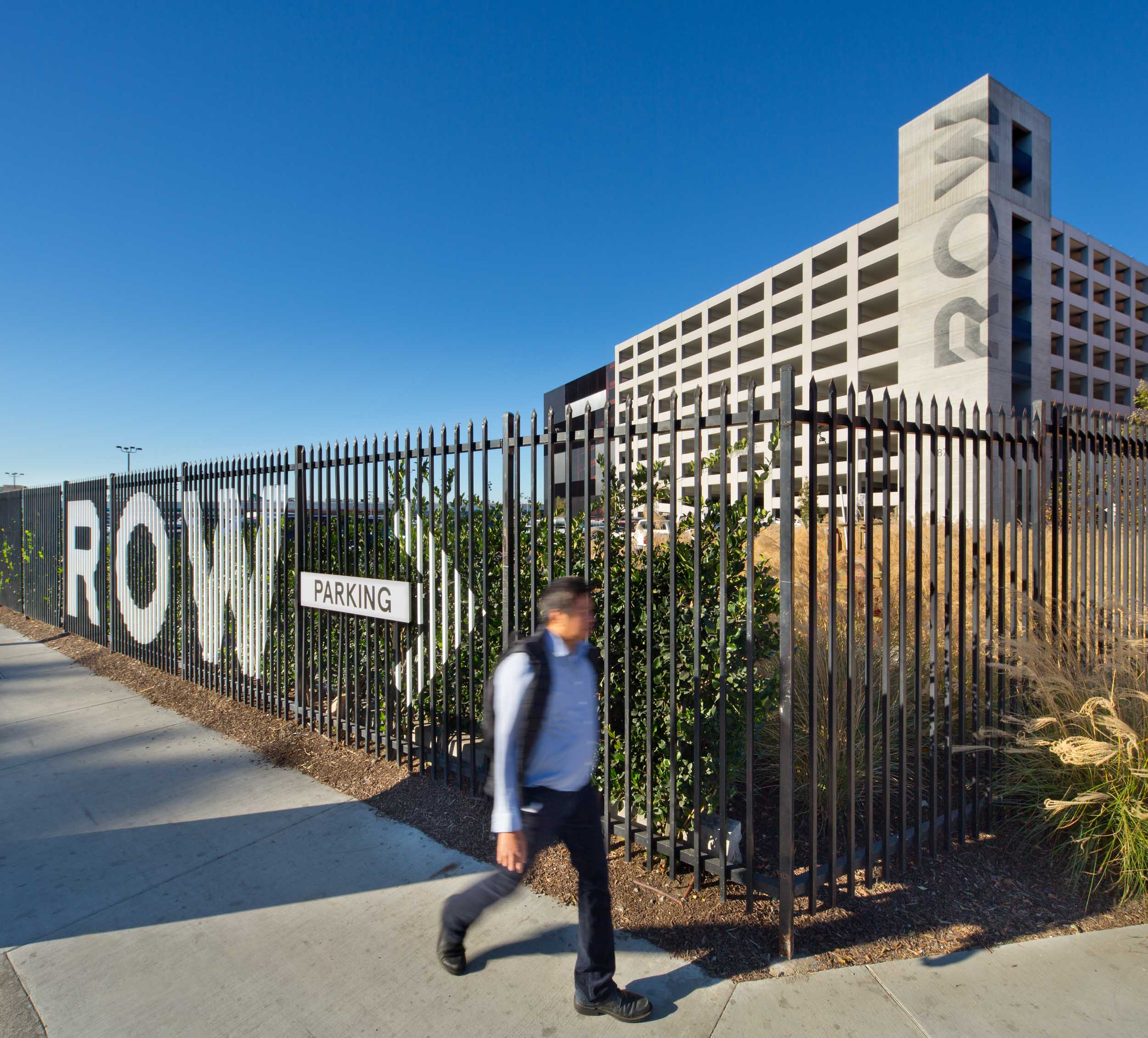 Man by fence with ROW and an arrow on it, with a building that has ROW printed down the façade