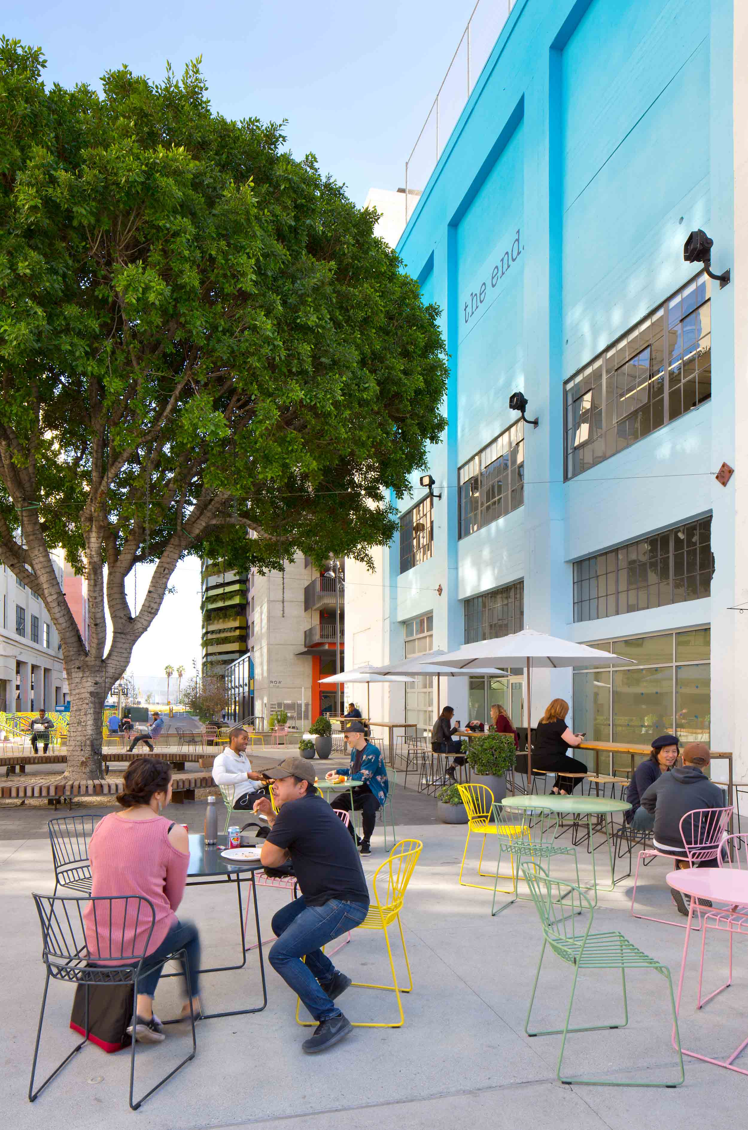 people seated at brightly colored chairs underneath a tree with "the end" written on a blue wall