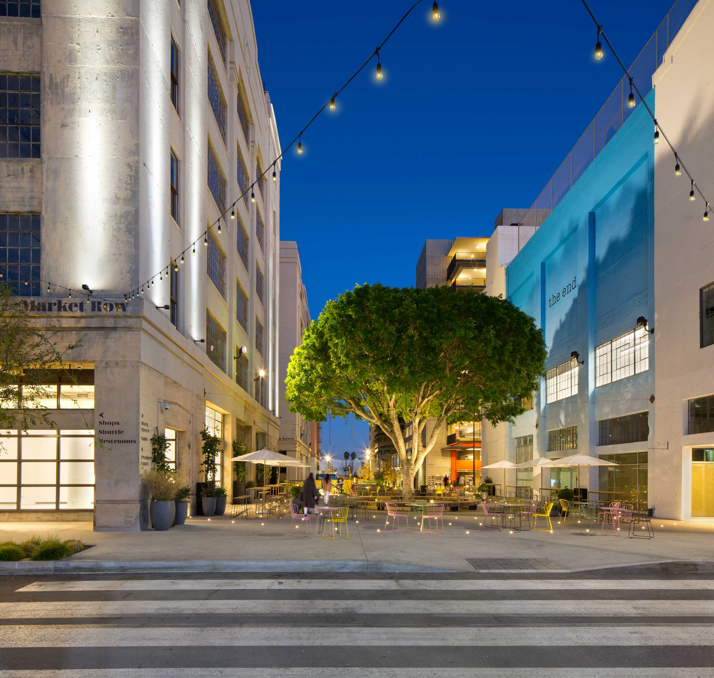 Large tree illuminated at night with people sitting at a table in the center of a courtyard