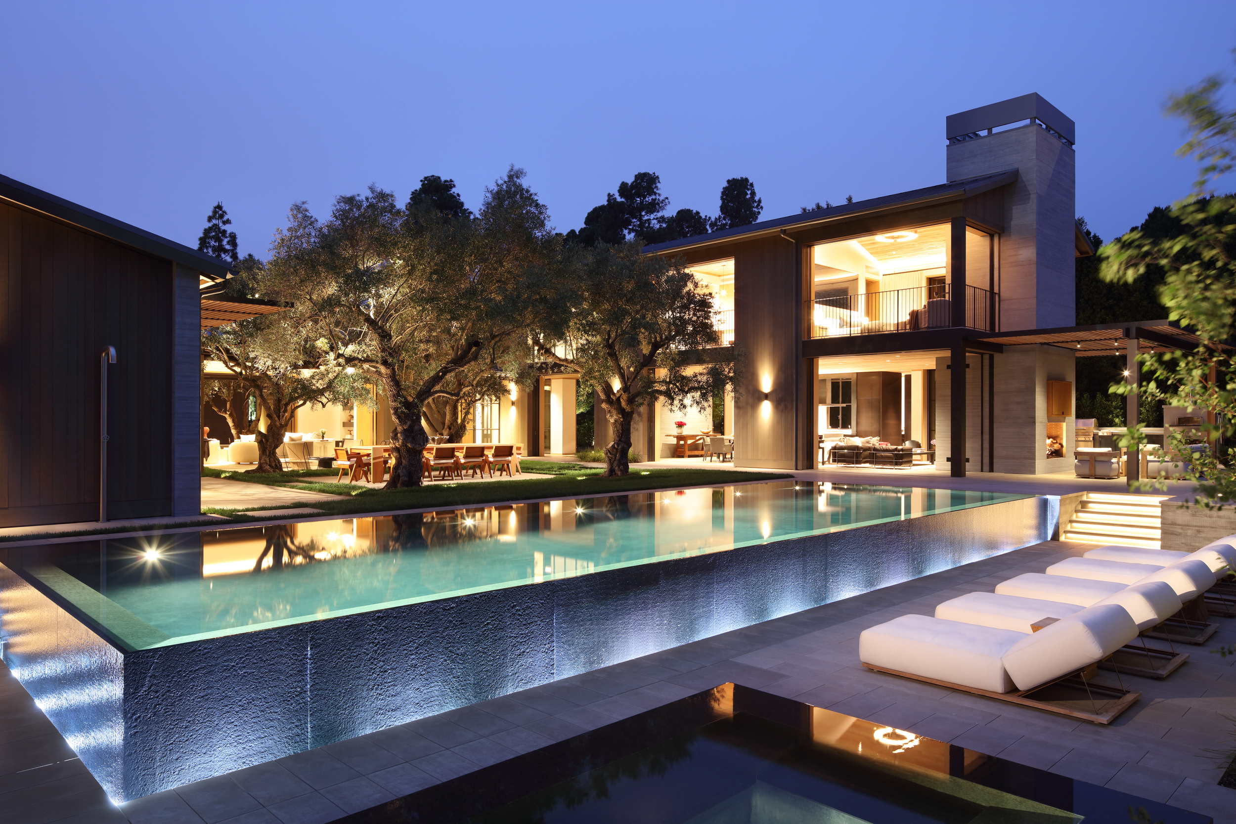 infinity pool and surrounding courtyard at dusk with lounge chairs