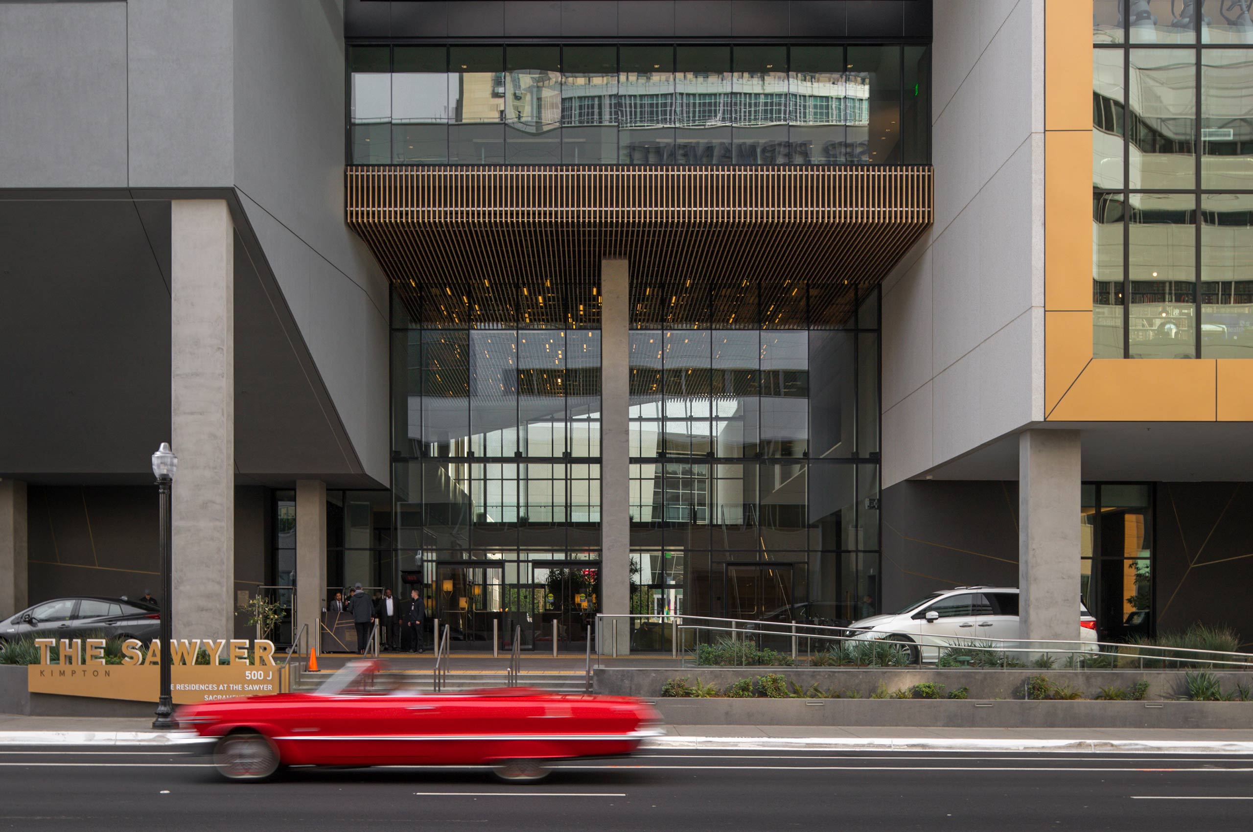 Kimpton sawyer hotel exterior street level view with red car driving by