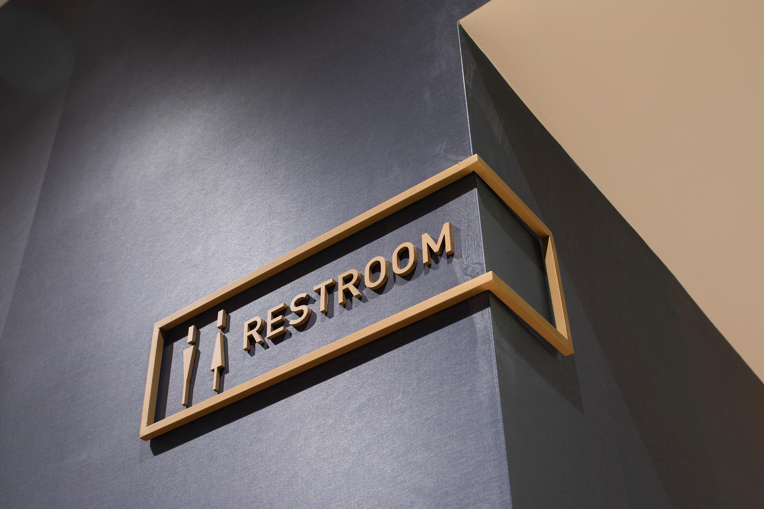 metal restroom sign wrapped around corner on dark grey wall