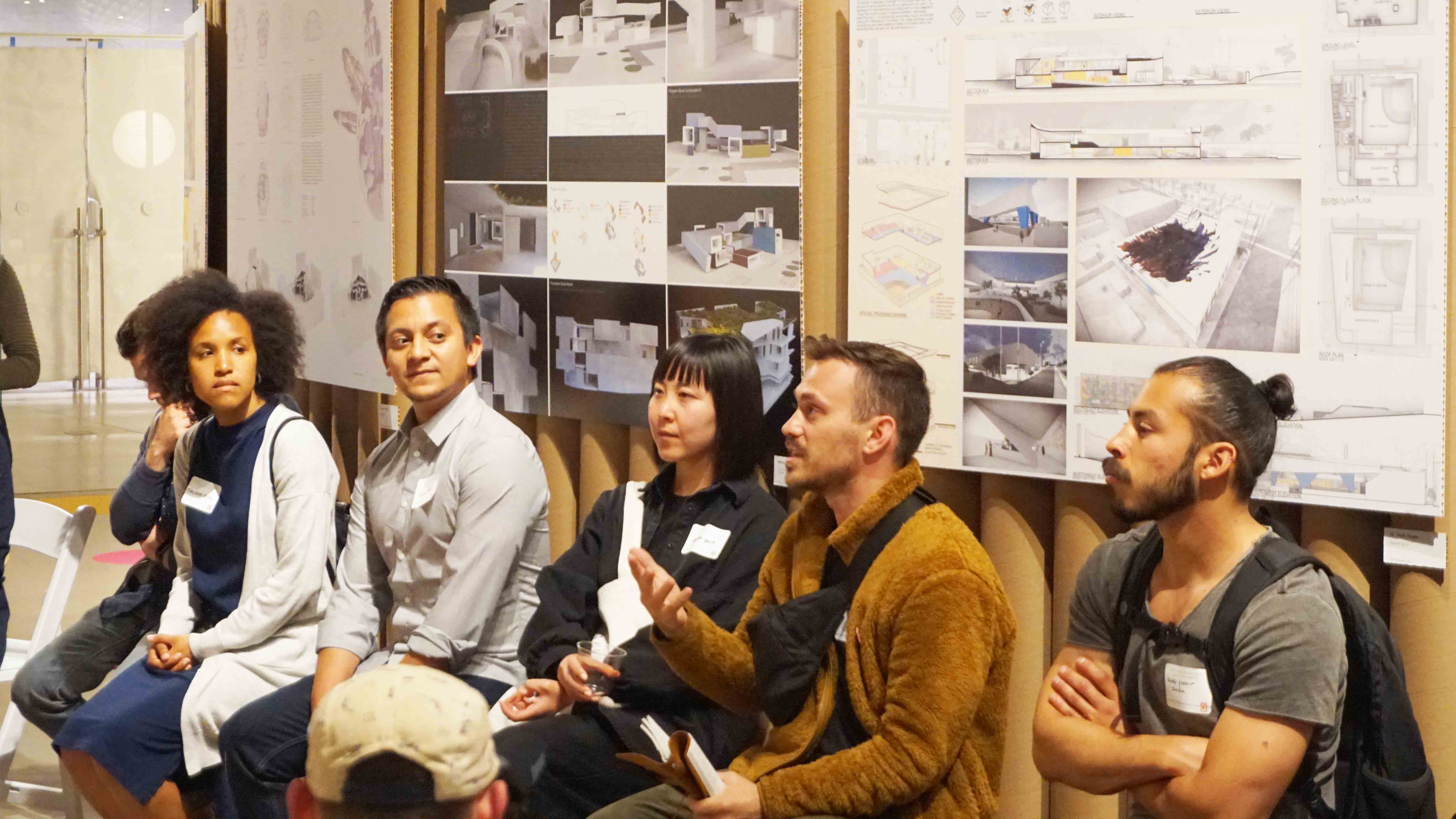 man speaking in a line of people in front of architecture plans