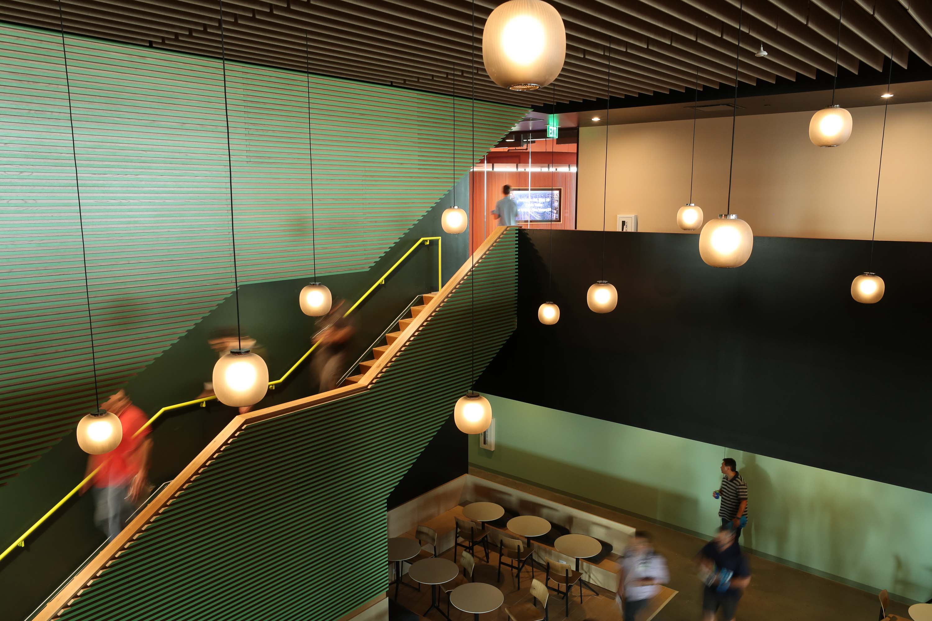 green stairs with people walking down and orb pendant lights hanging from the ceiling