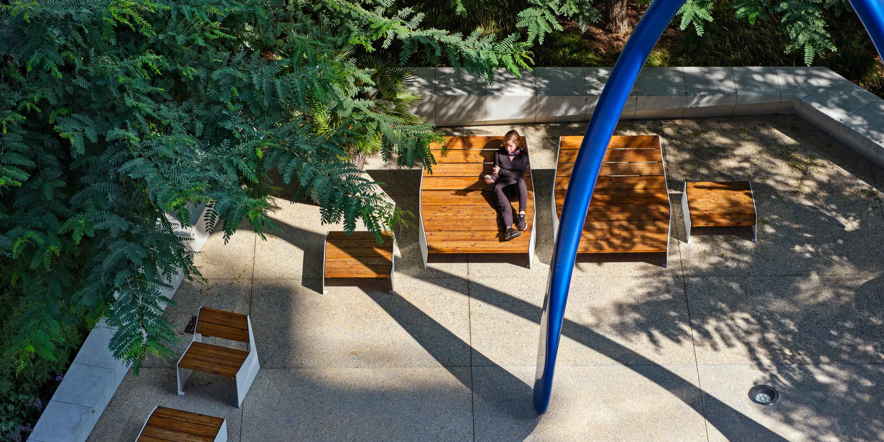 woman sitting on wooden lawn furniture under shade from a tree