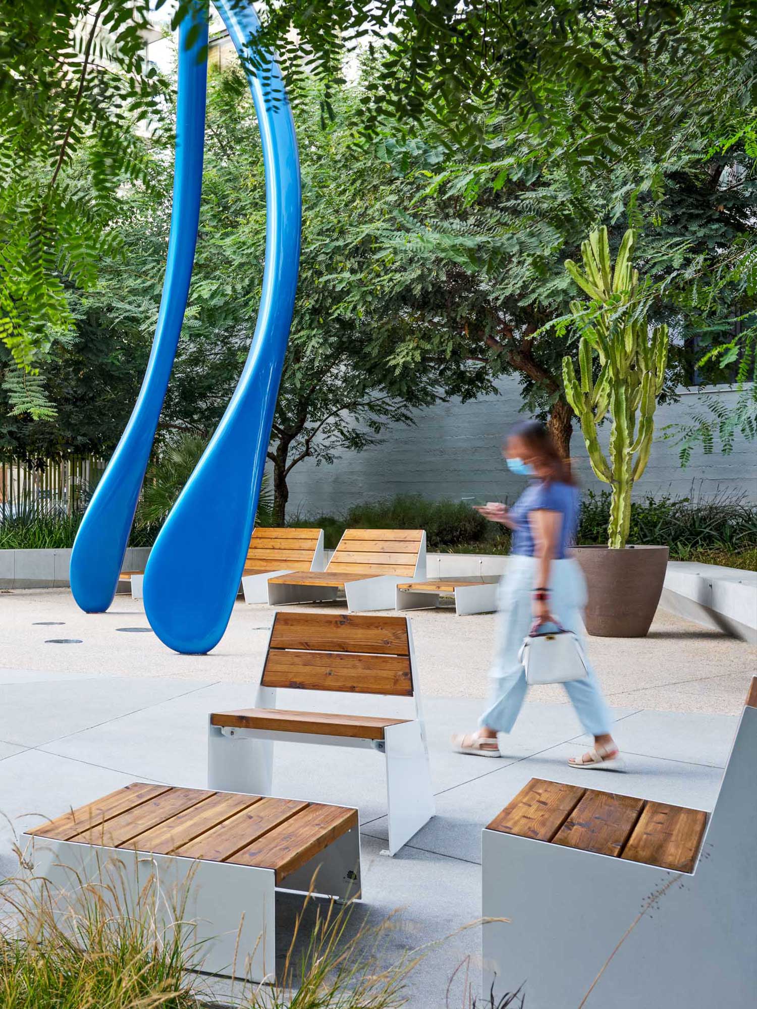 woman walking through a courtyard filled with wooden furniture and a large blue sculpture