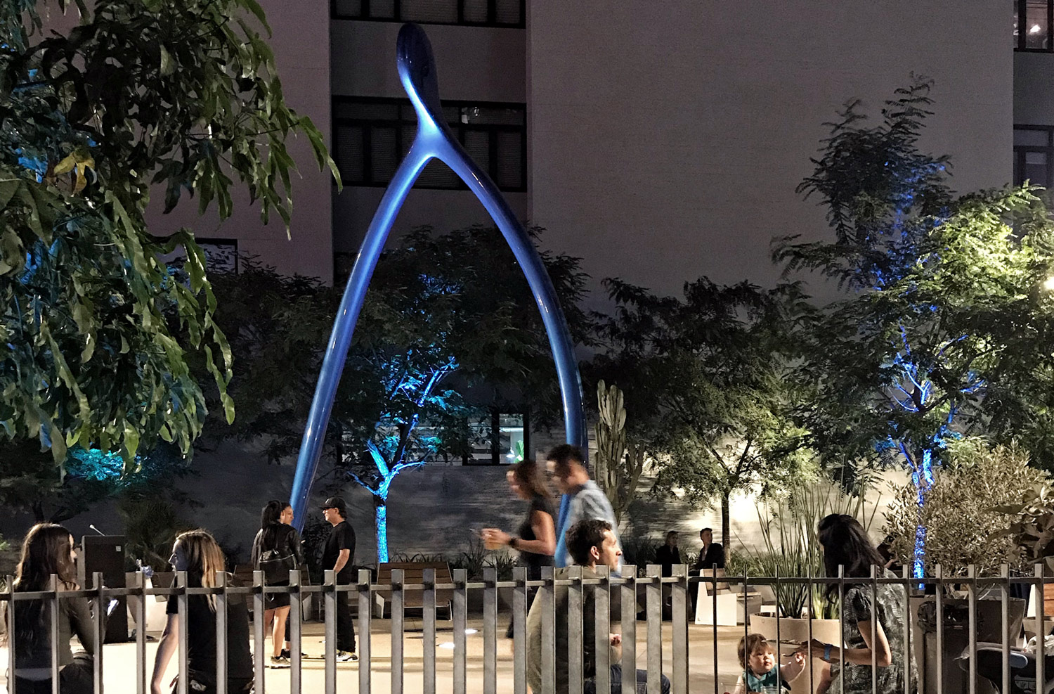 night shot of people in a courtyard with a large blue sculpture in the background