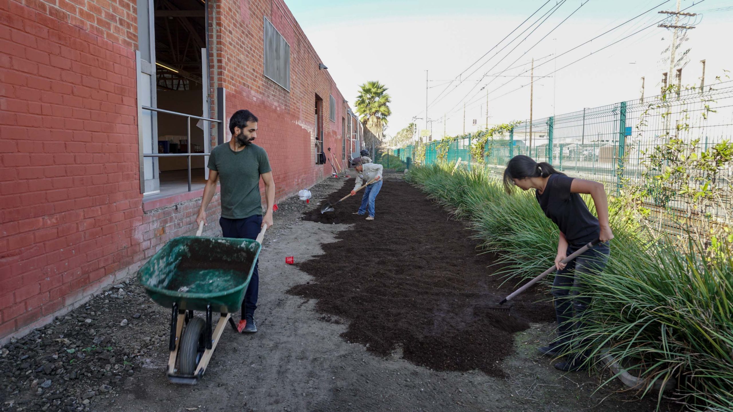 man with wheel barrow and woman raking soil