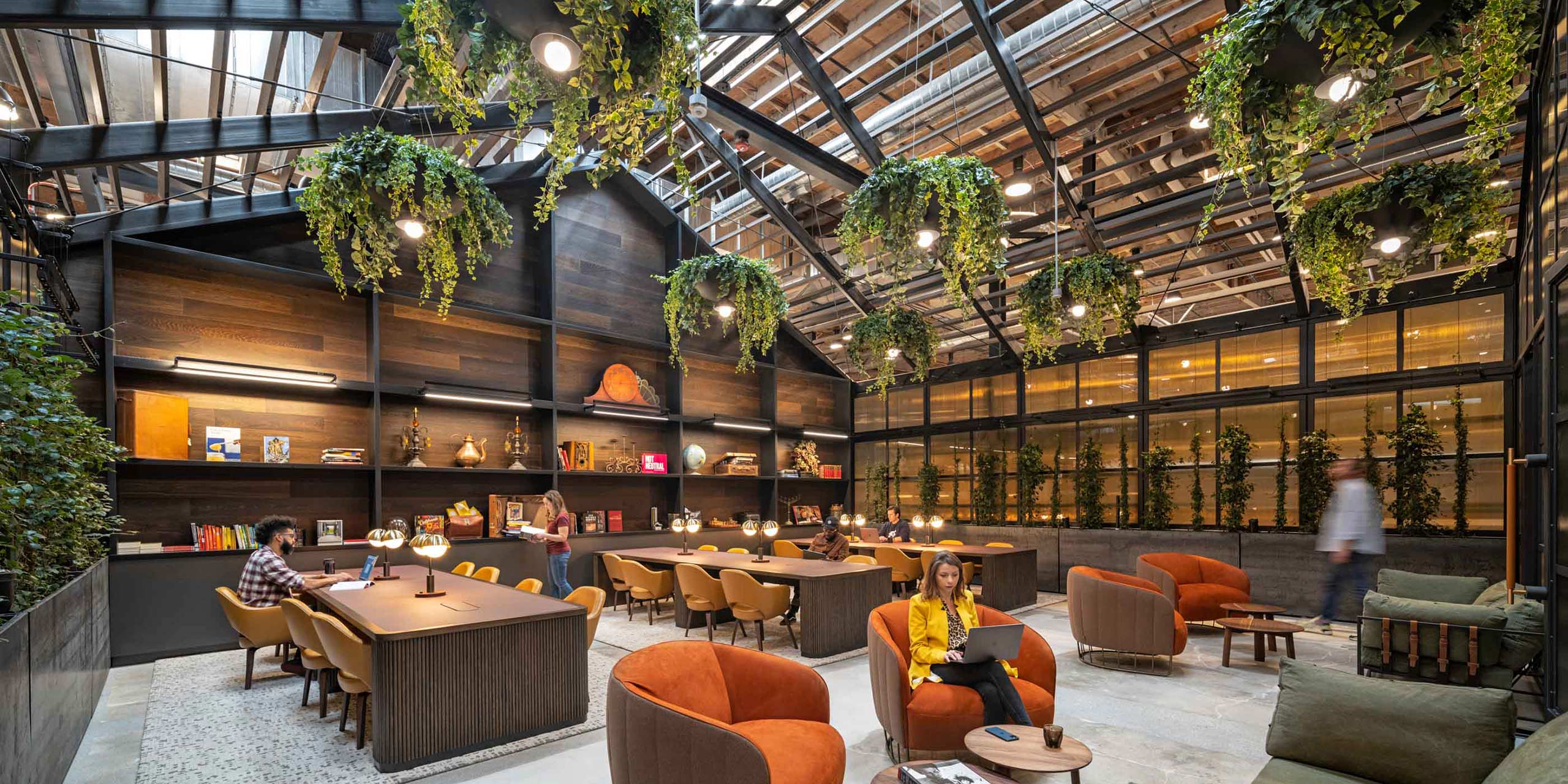 woman in a library with hanging plants on the ceiling with people working behind her