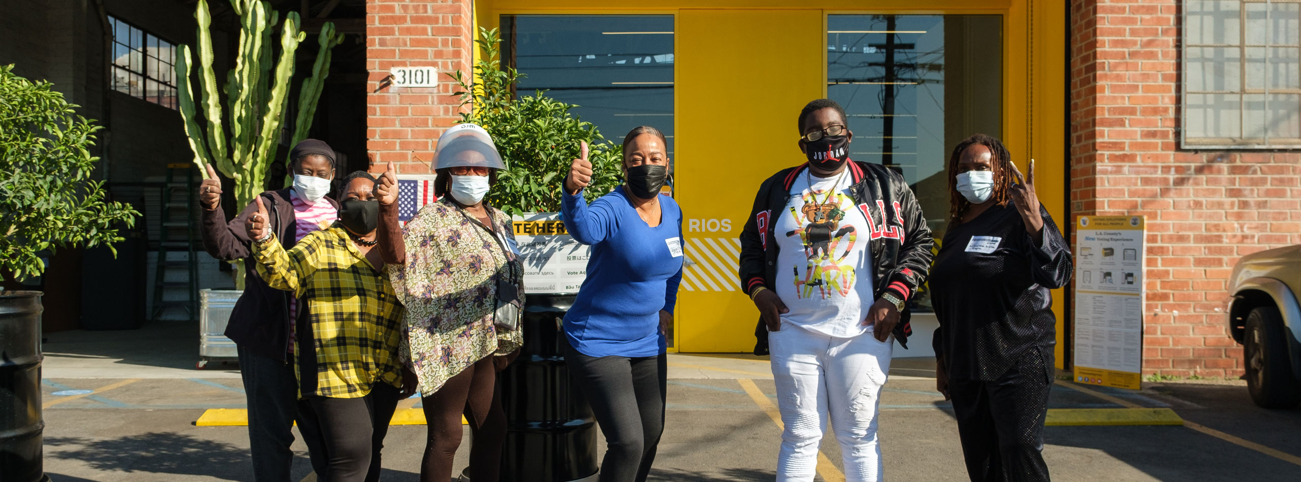 Los Angeles locals standing in front of the RIOS office wearing masks and giving a thumbs up