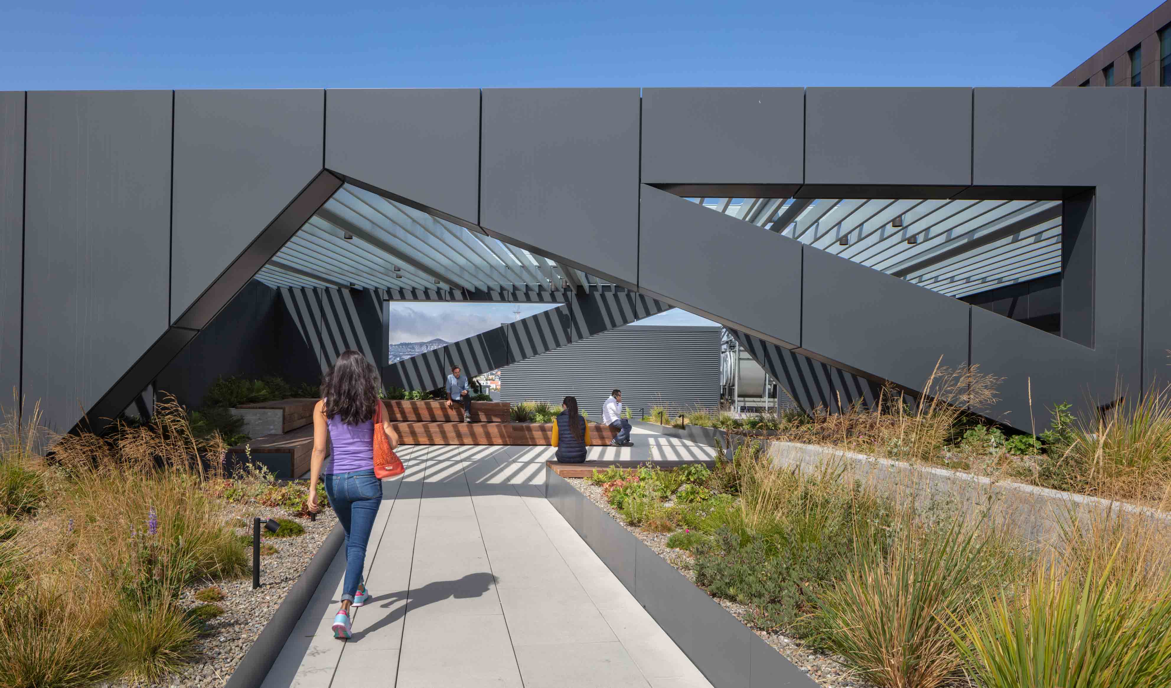 Women walking on a plant-lined sidewalk underneath a geometric arch