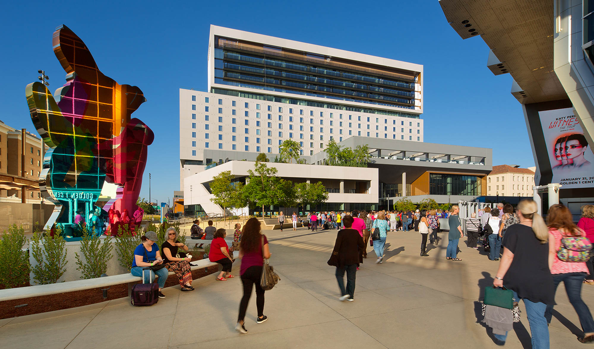 people walking in a plaza next to a metallic sculpture