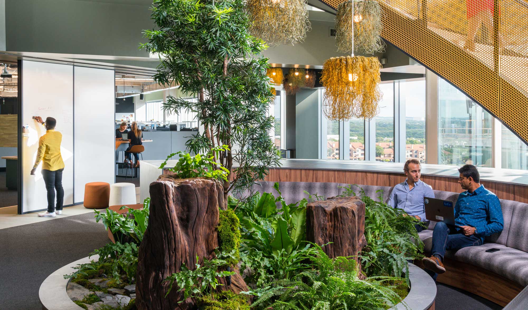 two people sitting on a bench behind an interior planter