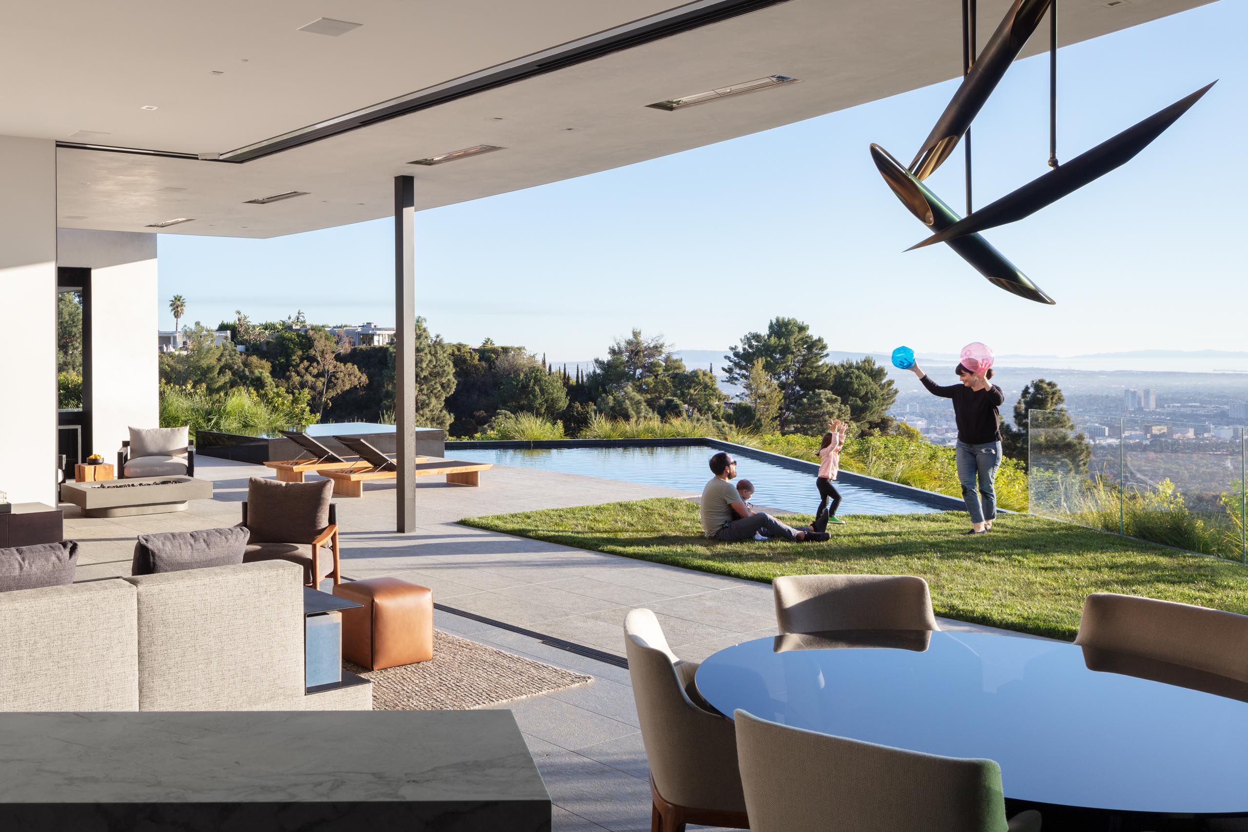 Seamless indoor to outdoor connection with glass walls opened and a family playing outside