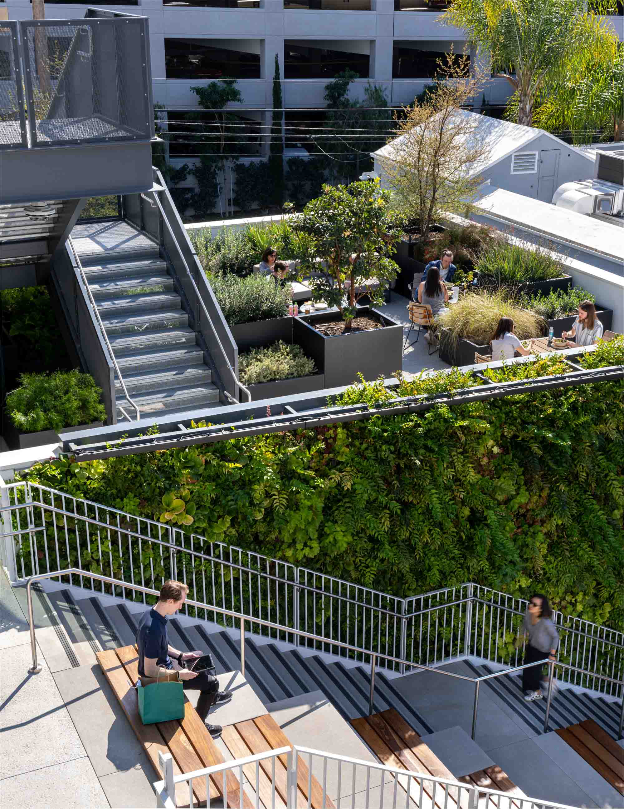 People eating and working outside on the stairway and exterior lounge areas adjacent to planters at Harlow