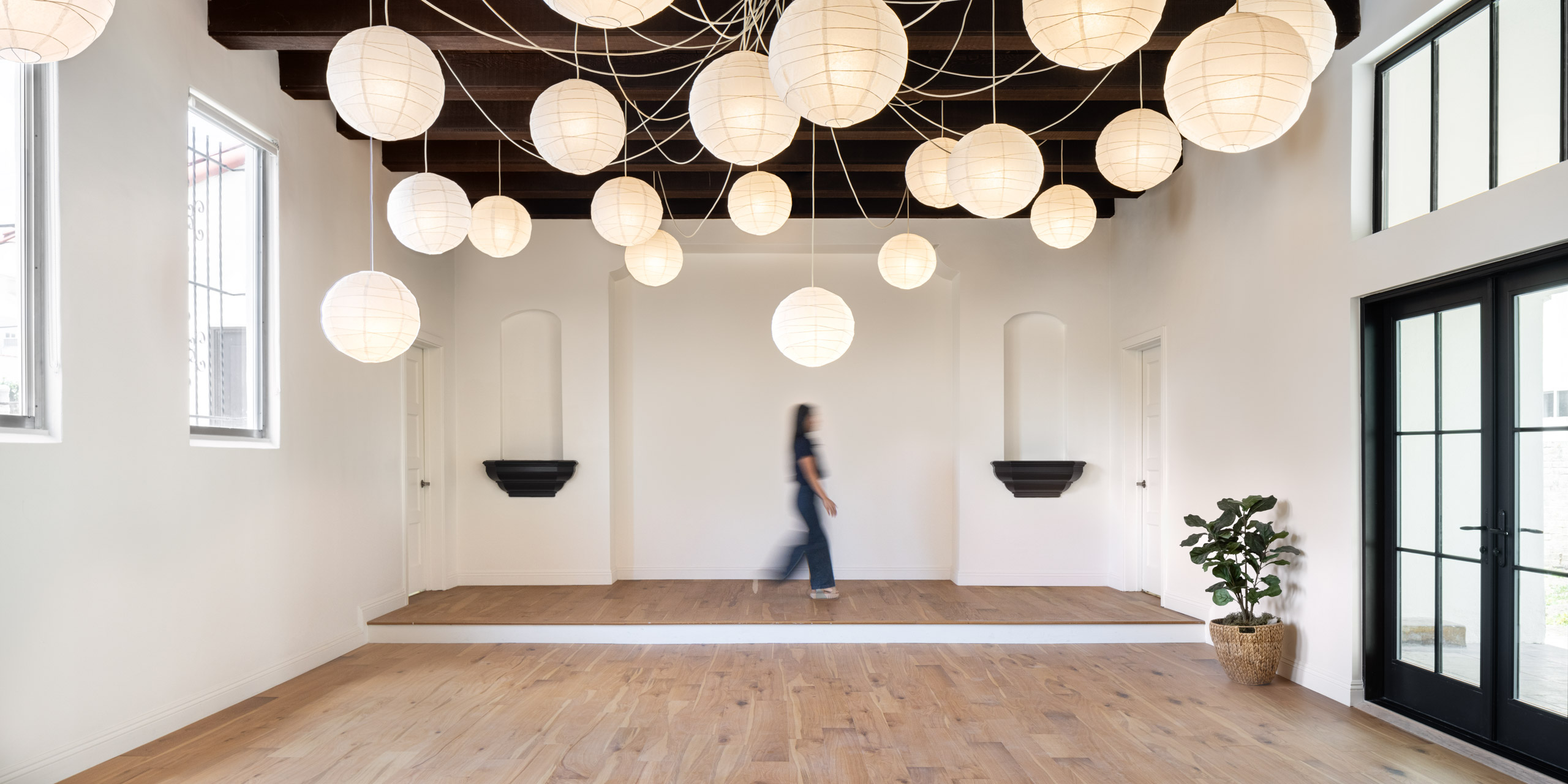 woman walking across spacious chapel room with wood floors, white walls, and lantern lighting