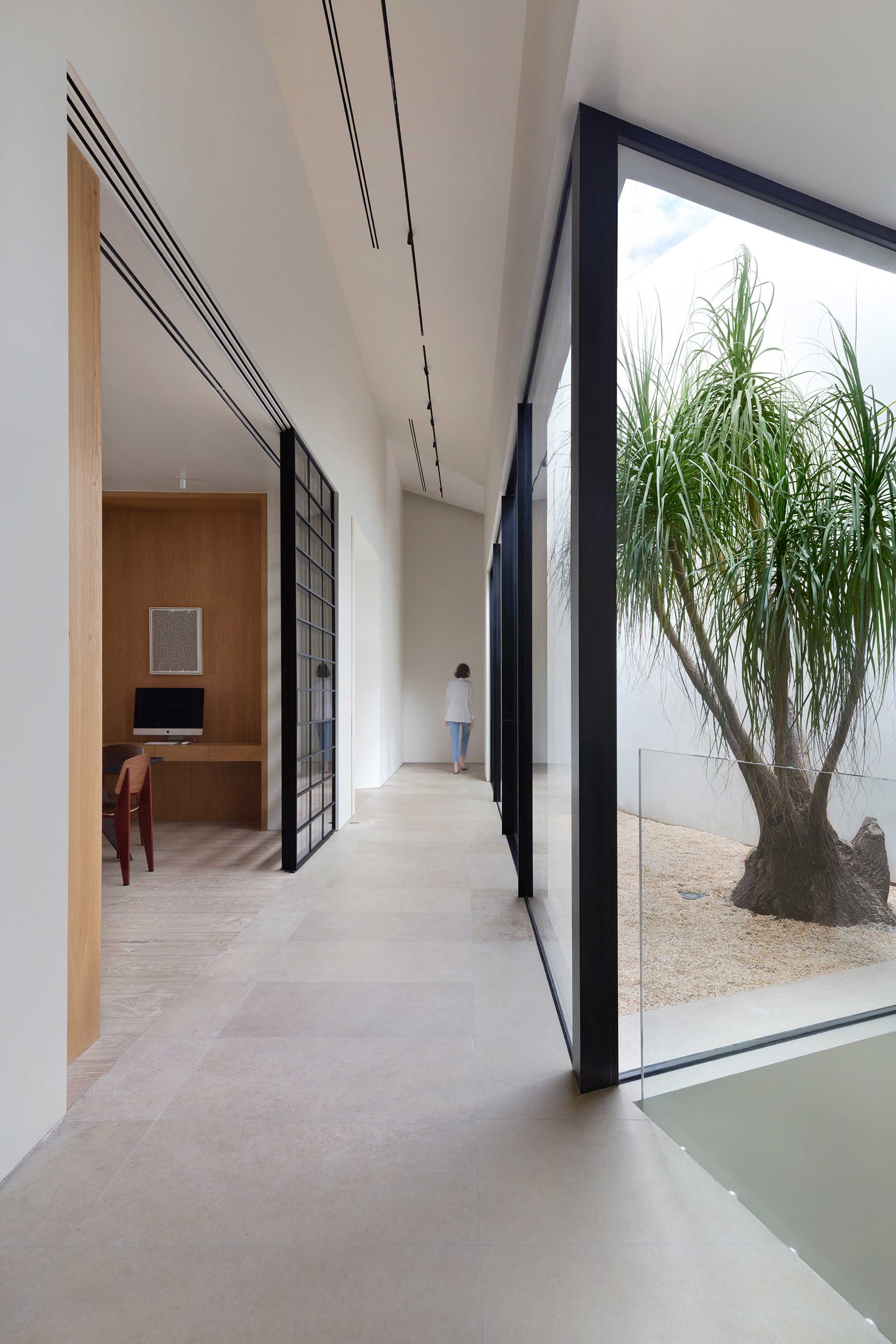 Woman walking hallway adjacent to large windows that reveal the interiors to the outdoor courtyard