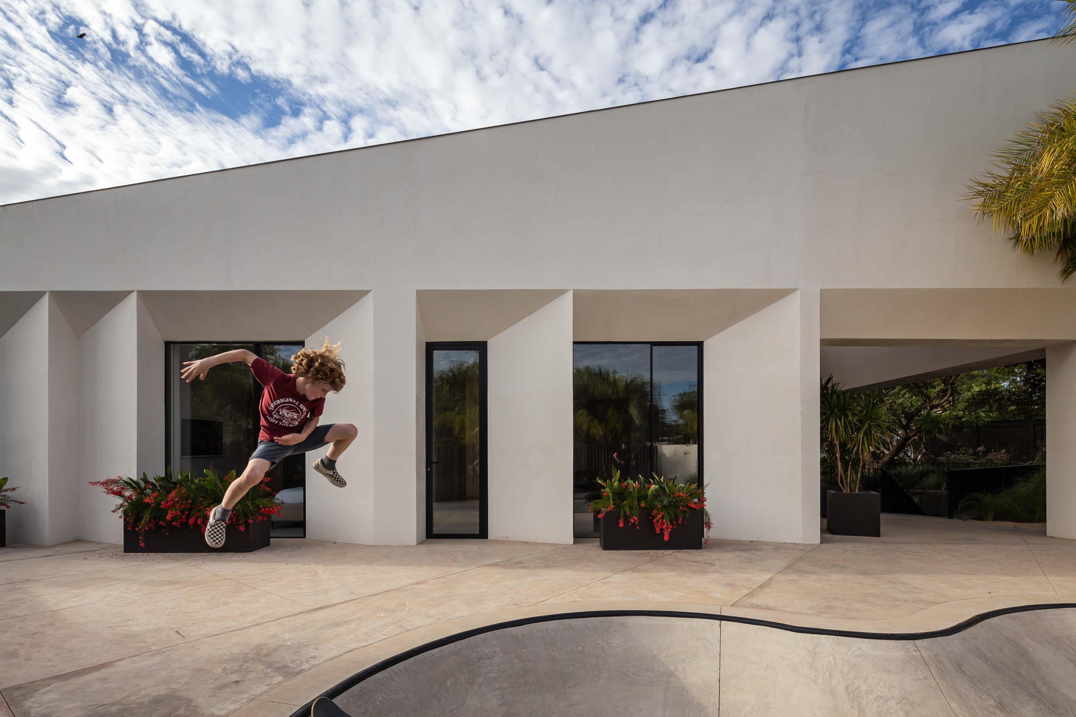 Boy jumping off his skateboard at the skate park with the home in the background